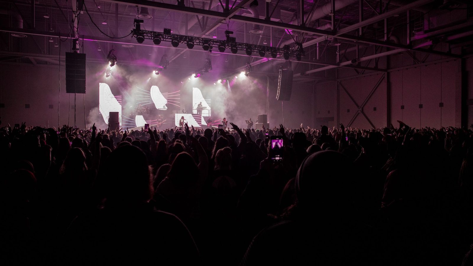 A packed arena crowd facing a lit concert stage